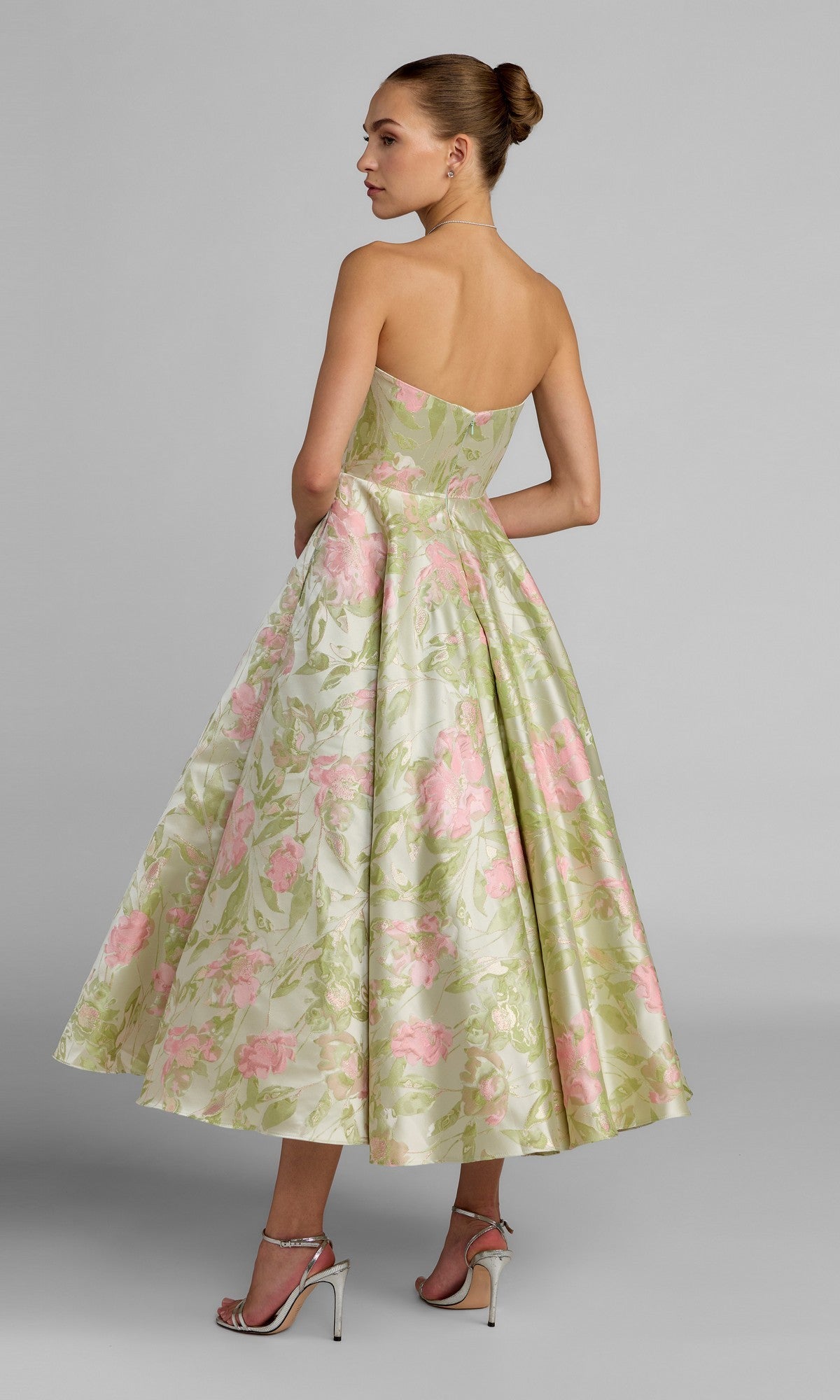 A woman stands in profile wearing the Mac Duggal 69147 Tea-Length Party Dress, featuring a strapless bodice and a full, floral skirt, paired with silver heels.